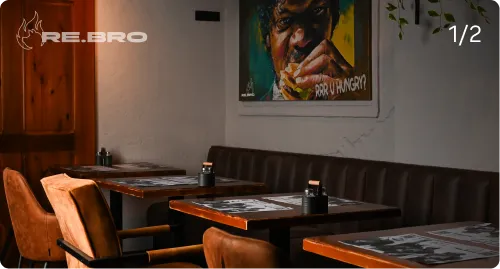 Empty restaurant seating with wooden tables, brown chairs, and a colorful portrait on the wall.