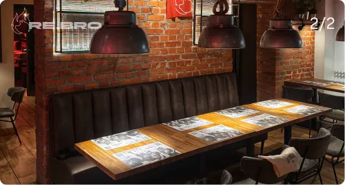 Cozy restaurant seating with long wooden table, cushioned bench, chairs, and hanging lamps against brick wall.