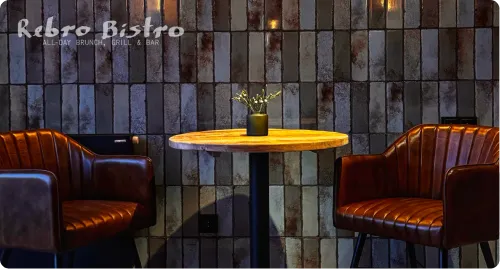 Two brown leather chairs with a round wooden table and small plant against a textured dark wall.