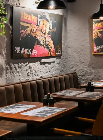 Cozy restaurant booth with brown seating, wooden tables, menus, and wall art featuring ribs.