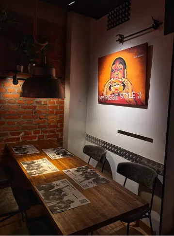 Cozy dining area with a wooden table, chairs, placemats, brick wall, and a lit painting of a person eating burger.