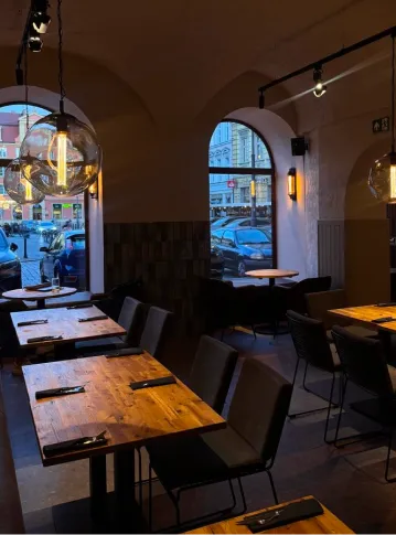 Interior of dimly lit restaurant with wooden tables, black chairs, and large glass pendant lights.