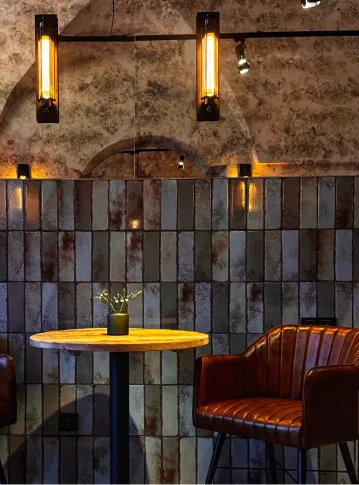 Cozy seating with brown leather chair, wooden table, small plant, and warm wall lights in a rustic setting.