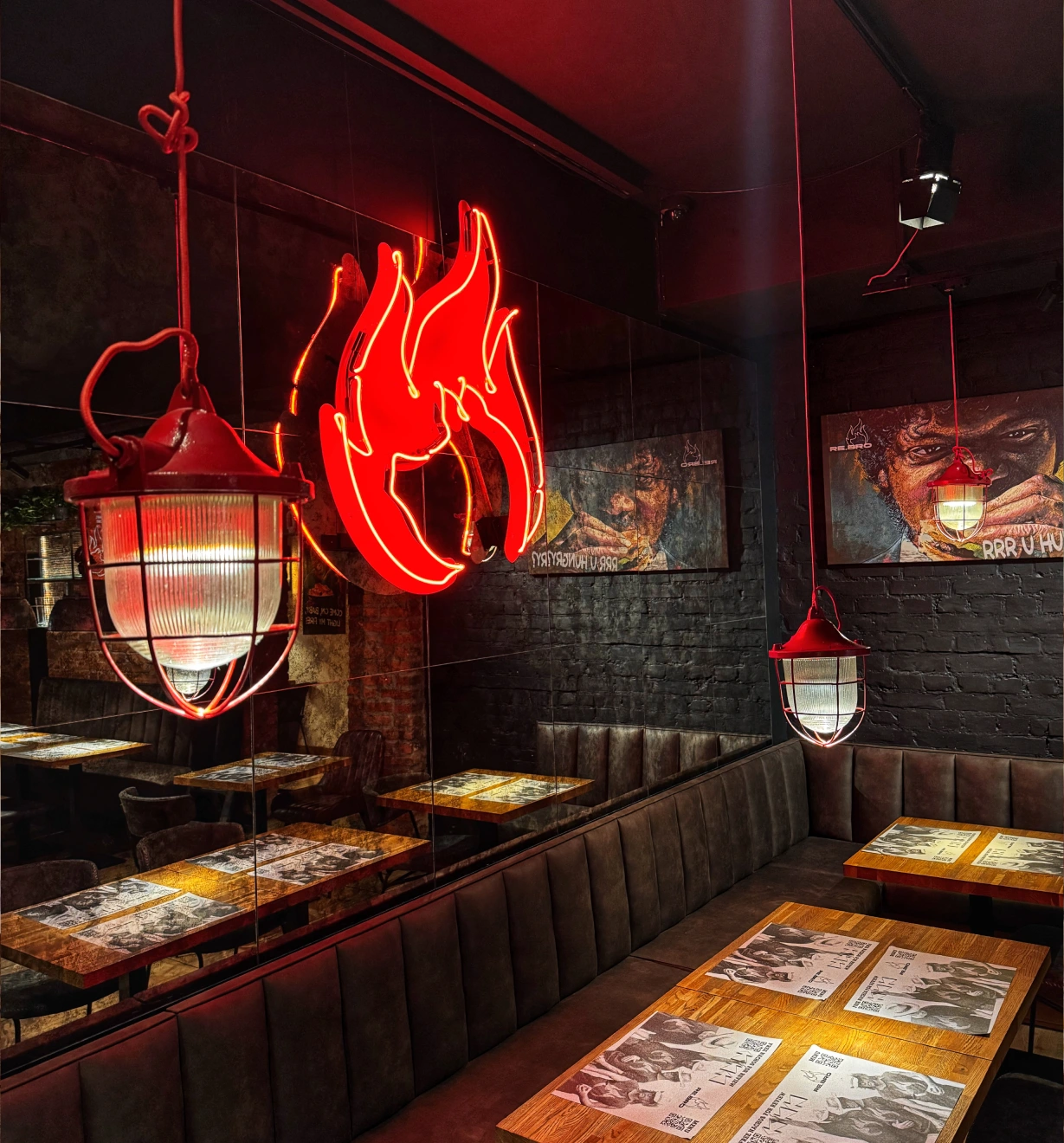 Cozy restaurant corner with leather seating, wooden tables, hanging cage lamps, and red neon flame sign.