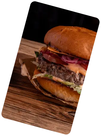 Close-up of a hamburger with beef patty, lettuce, tomato, onions, and sauce on a wooden surface.