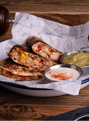 Grilled chicken quesadillas with corn and red peppers served with sour cream and guacamole dips.