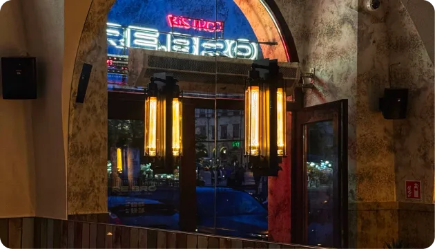 Warm lit hanging lamps reflected in a window with neon signs and street scene outside at night.