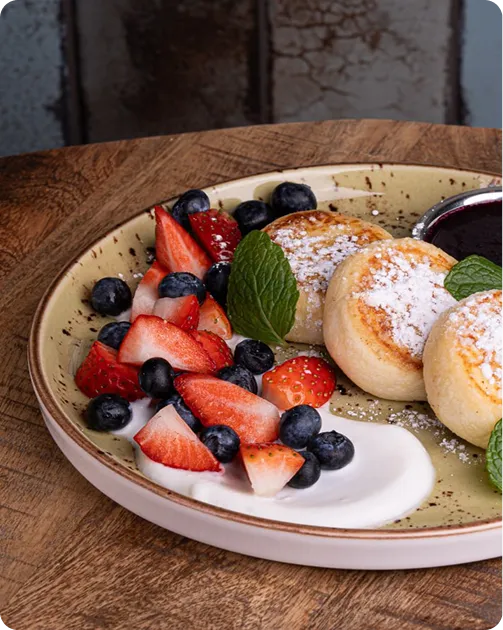 Plate with fried cheese pancakes, fresh strawberries, blueberries, cream, mint, and berry sauce.