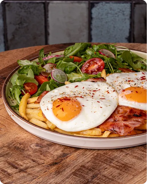 Plate with two fried eggs, bacon, fries, and fresh green salad with cherry tomatoes and radishes.