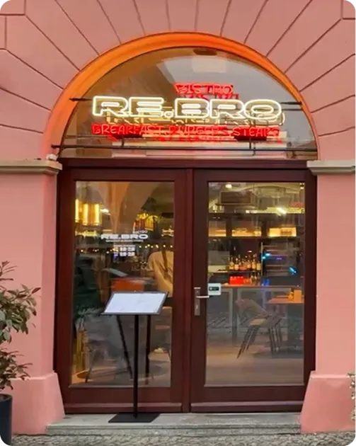 Entrance of a restaurant with glass doors, neon sign reading RE.BRO, and menu stand outside.