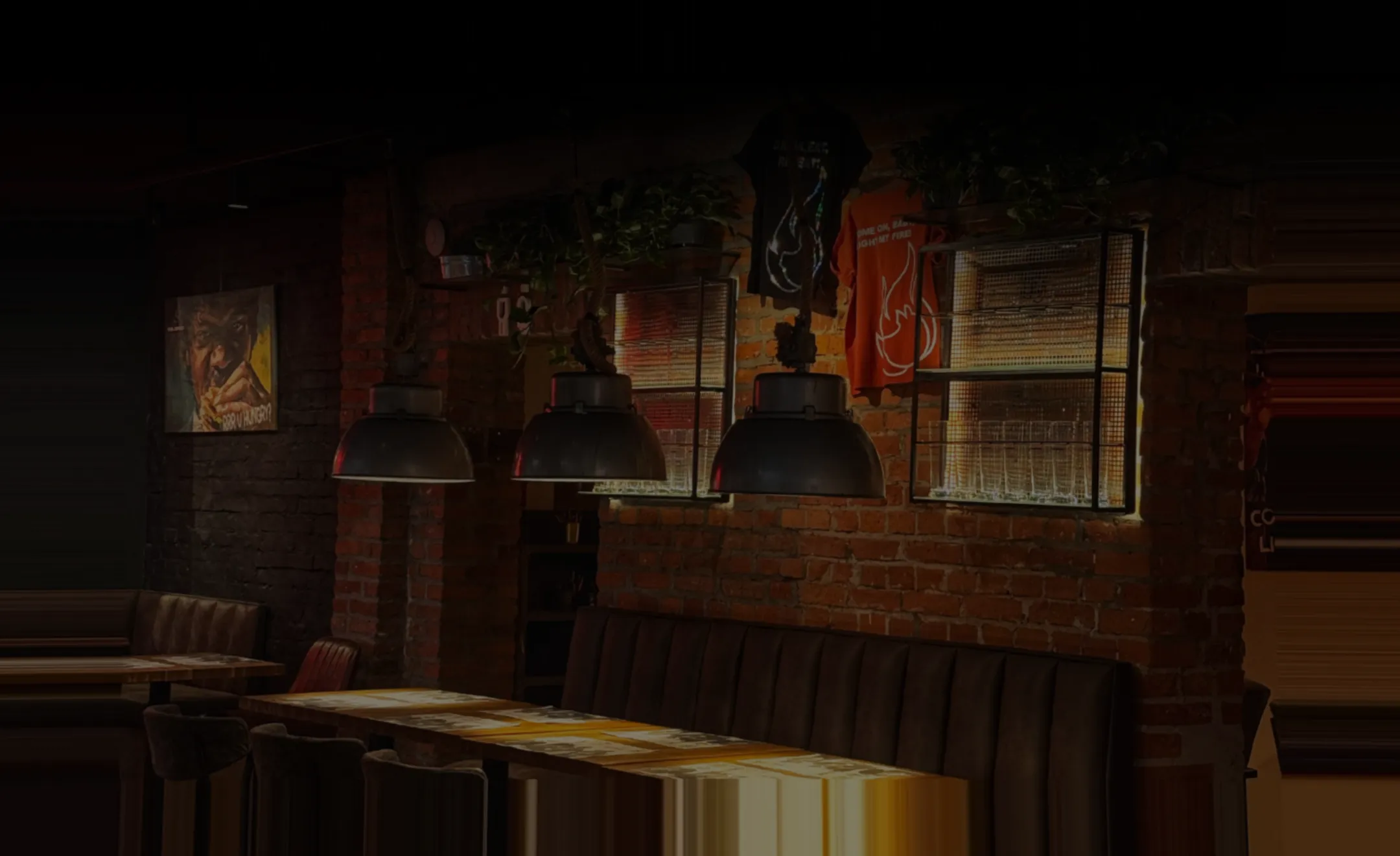 Cozy restaurant interior with brick walls, leather seating, hanging lamps, and wall art.