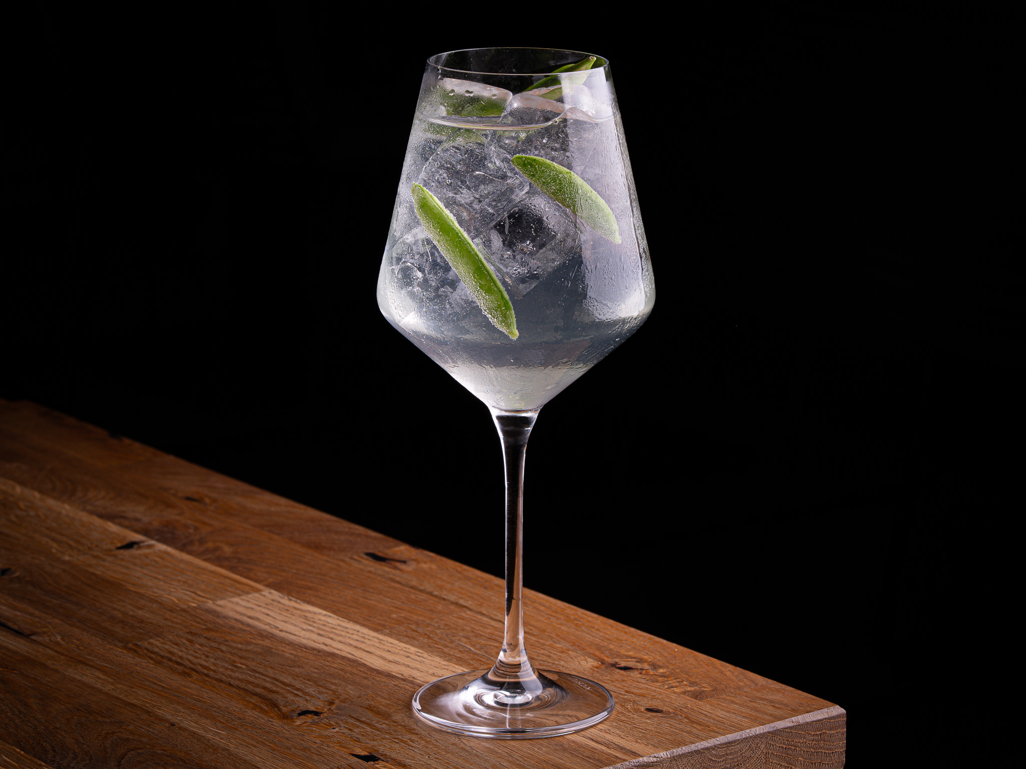Clear cocktail in a coupe glass garnished with a small red flower, on a wooden surface.