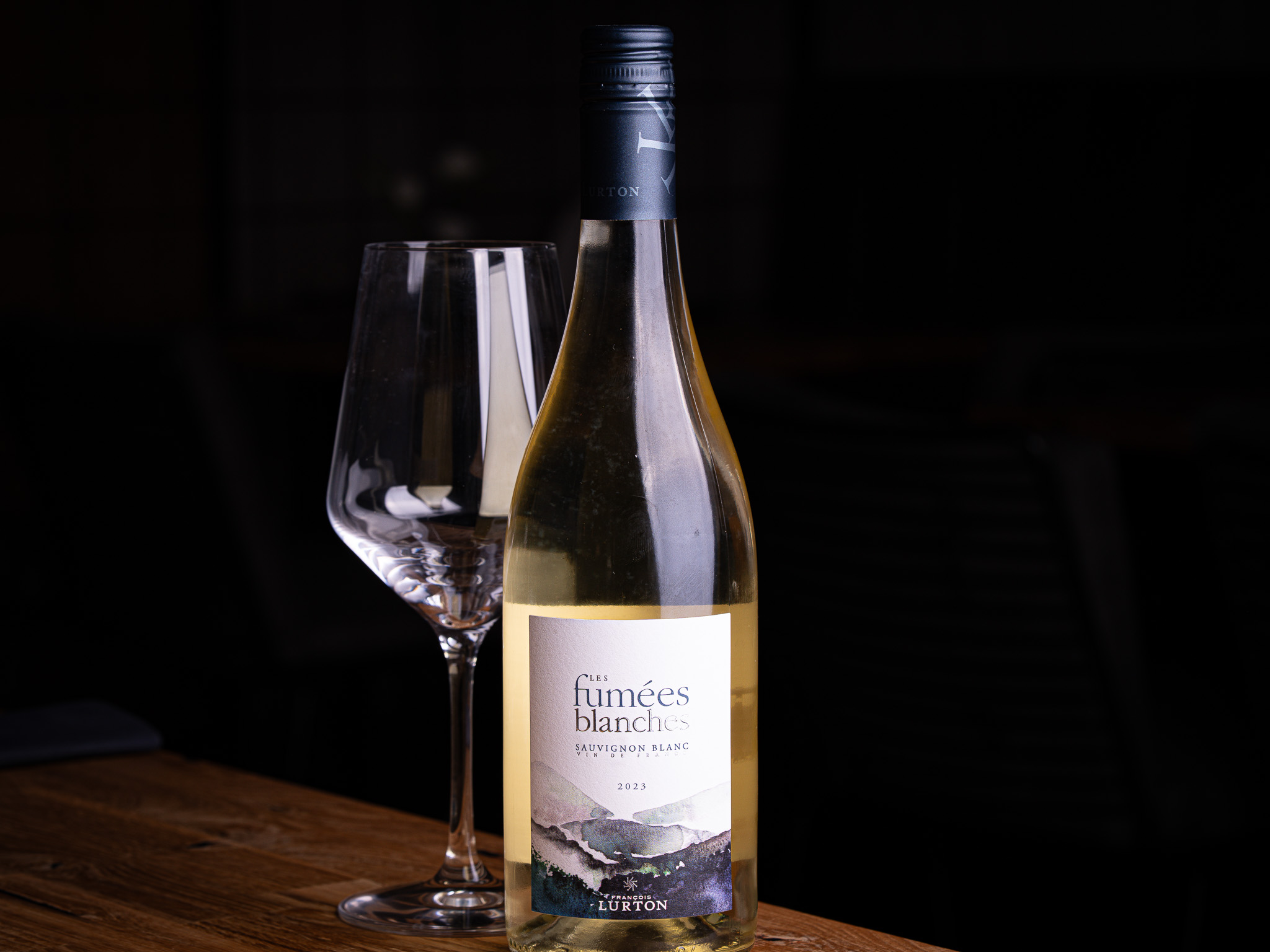 A bottle of La Linda red wine and an empty wine glass on a wooden surface against a black background.