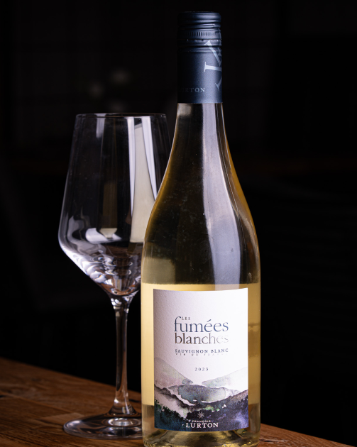 Bottle of La Linda red wine and empty glass on a wooden surface with dark background.