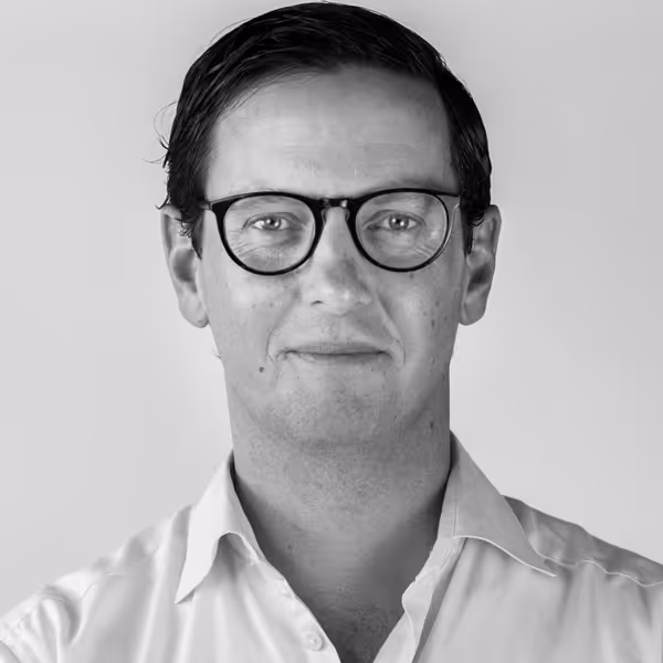 Black and white headshot of a man with short dark hair, glasses, and a white collared shirt.