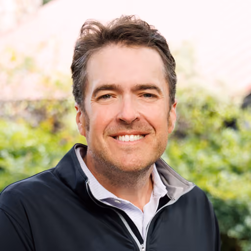 James Avery smiling with short brown hair wearing a dark jacket outdoors with greenery in background.