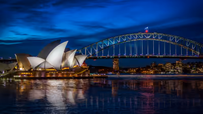 Sydney Opera House and Sydney Harbour Bridge illuminated at dusk with reflections on the water.