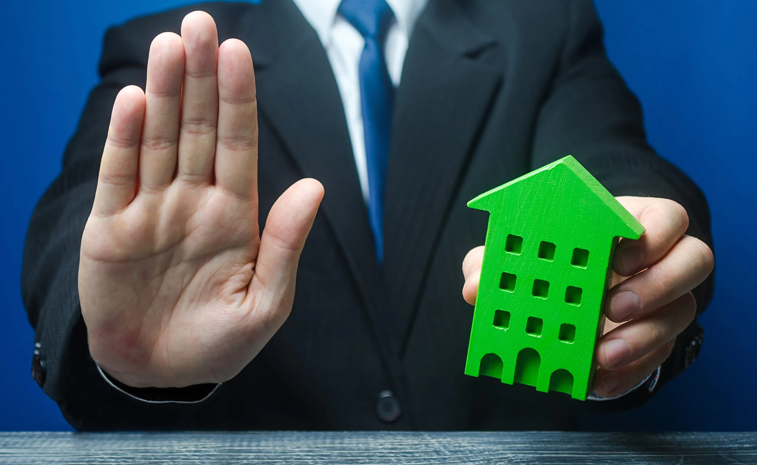 Man with a green house makes a stop gesture. Bank refusal to provide a mortgage loan. Housing problems, unscrupulous dishonest company builder. Confiscation pledged property. Refusal residence permit.