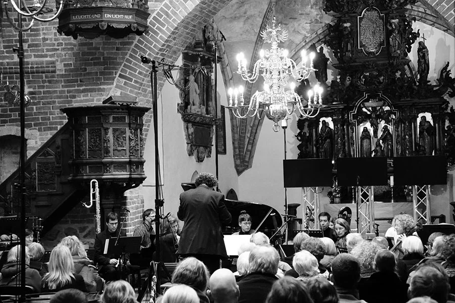 Dirigent leitet ein Orchester mit Musikern und Publikum in einer historischen Kirche.