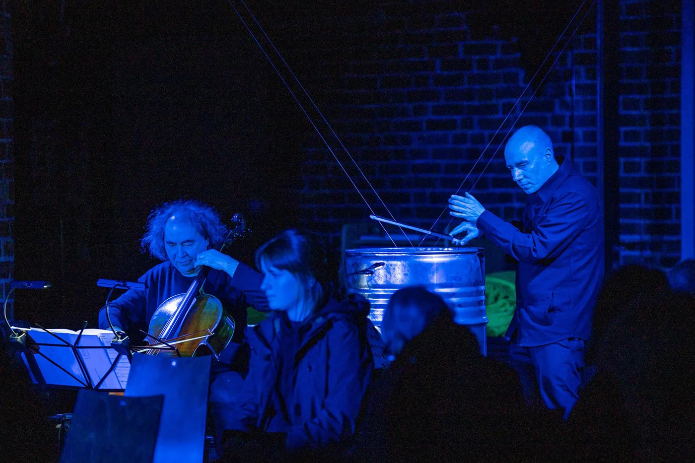 Drei Musiker bei einem blauen Lichtkonzert, einer spielt Cello, ein anderer Schlagzeug.