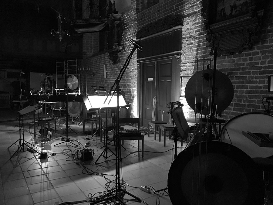 Schwarzweißaufnahme von Musikinstrumenten, Mikrofonständern und Stühlen in einem Backsteingebäude.