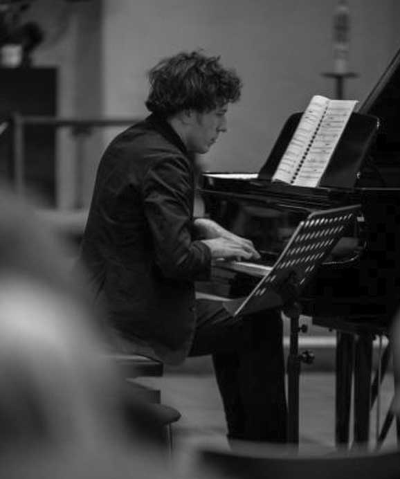 Ein Musiker spielt konzentriert Klavier mit Notenblatt im Hintergrund in Schwarz-Weiß.
