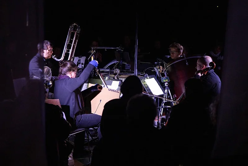 Orchestermusiker spielen im Dunkeln mit beleuchteten Notenständern bei einem Konzert.