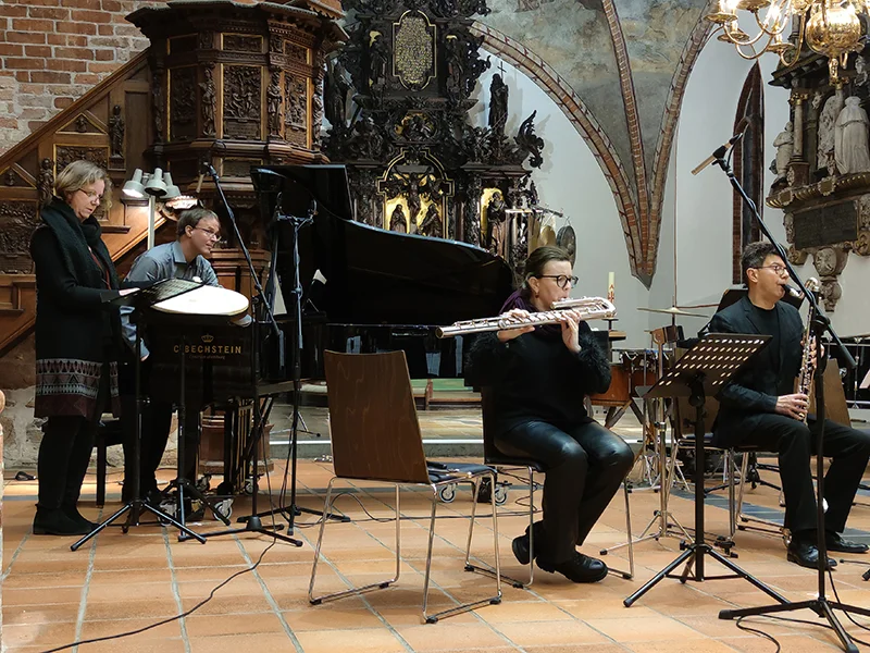 Vier Musiker spielen Klavier, Querflöte, Klarinette und Schlagzeug in einer Kirche.