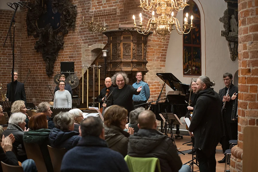 Musiker in einem Raum mit Backsteinwänden verneigen sich vor applaudierendem Publikum.