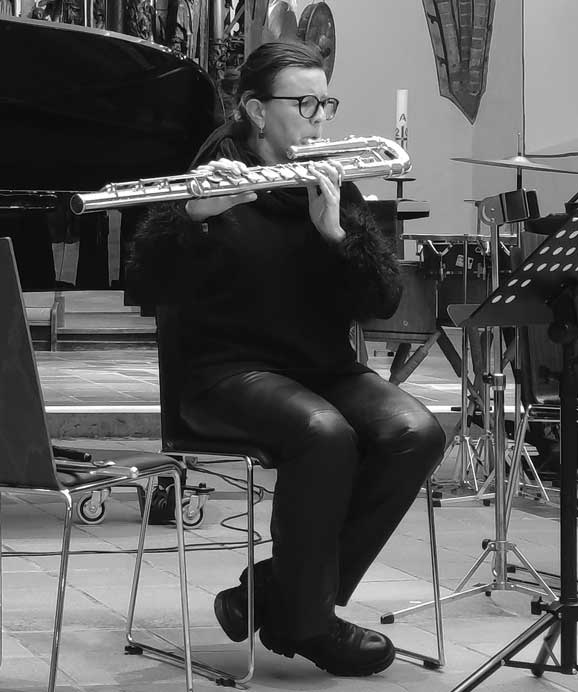 Eine Frau sitzt und spielt Querflöte in einem Raum mit musikalischen Instrumenten.