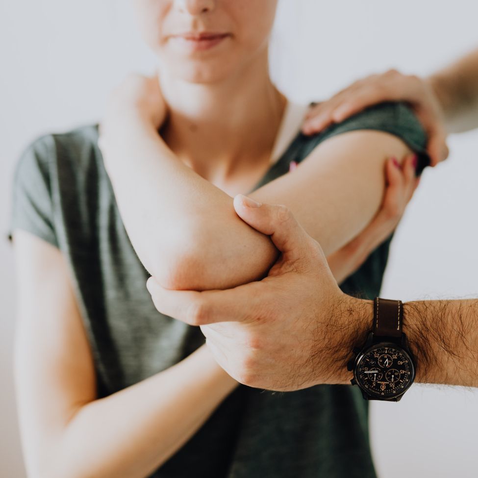 A person in a gray shirt is receiving an arm stretch or physical therapy on their elbow from another person.