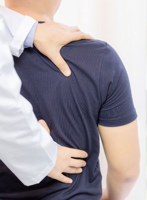 Hands of a healthcare professional examining a patient's back wearing a dark blue shirt.