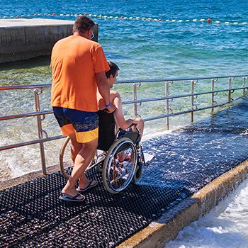 A caregiver pushing a client down a wheelchair ramp to enjoy the water.