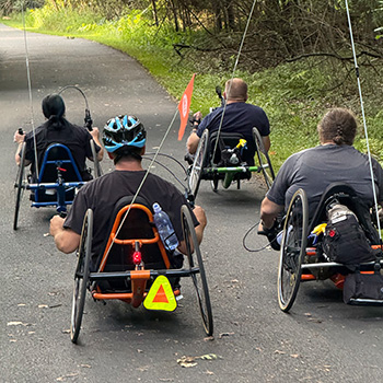 a group hand cycling on a paved path in the woods