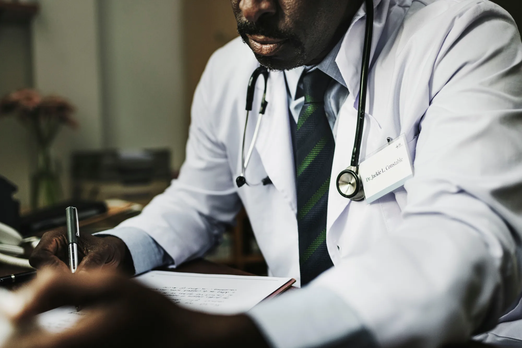 A doctor in a white coat writing notes at his desk
