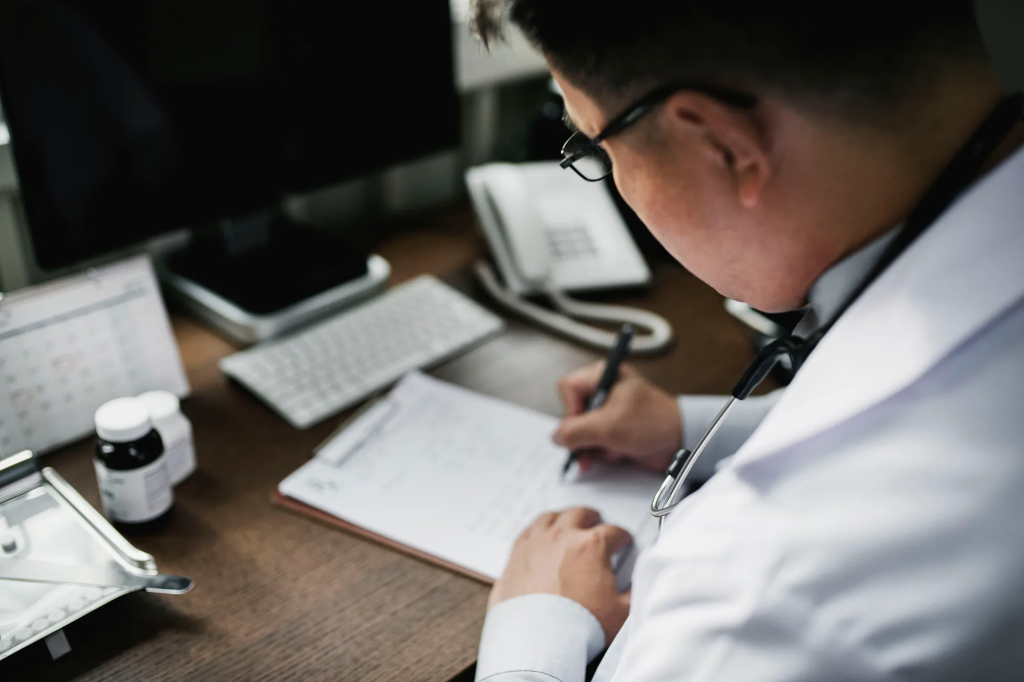 A physician in a white coat writing notes at a desk