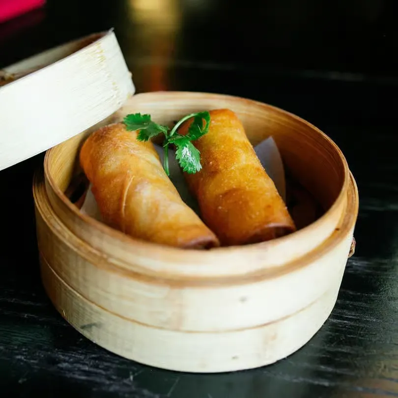 Two golden fried spring rolls garnished with parsley in a bamboo steamer basket.