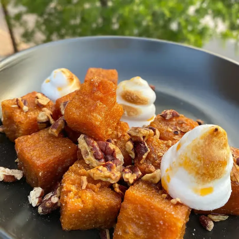 Plate of roasted sweet potato cubes topped with toasted marshmallows and pecan pieces.