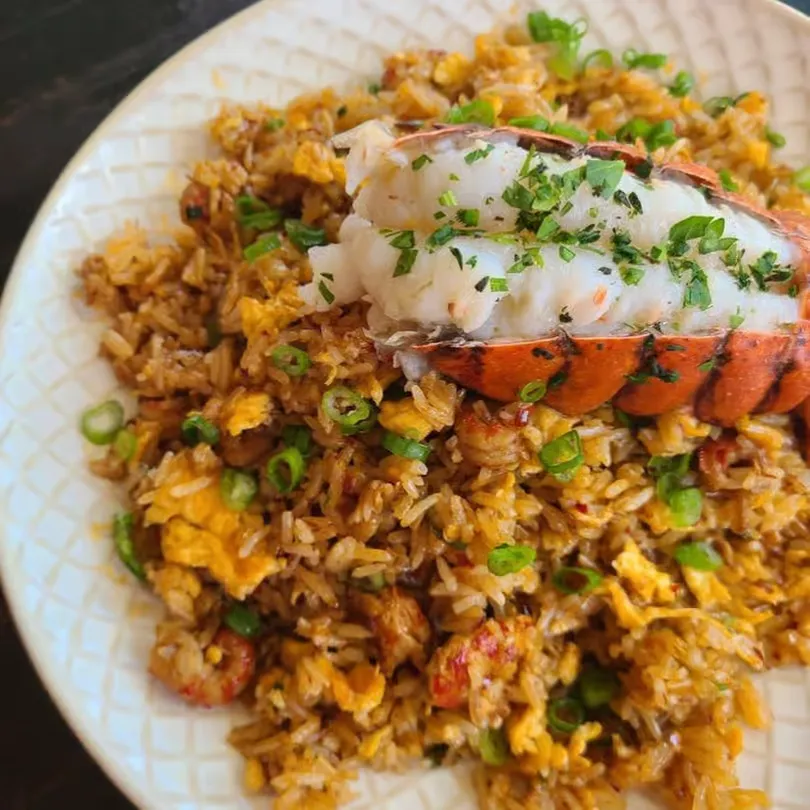 Plate of fried rice with scrambled eggs, green onions, and a lobster tail garnished with herbs.