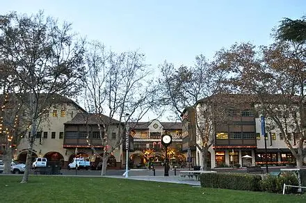 Town square buildings with lights wrapped on trees and a clock tower at dusk.
