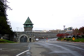 Stone prison gate with a guard tower and road leading up to it on a cloudy day.