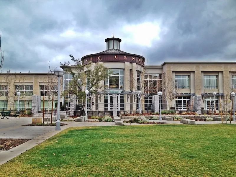 Modern public building with circular glass entrance, stone pillars, and a green lawn under cloudy sky.