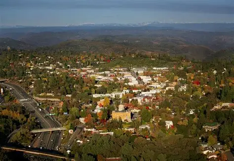Aerial view of a small town surrounded by trees and hills with a highway on the left side.