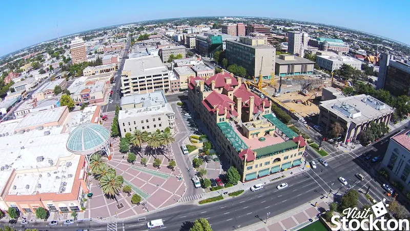 Aerial view of downtown Stockton, showing buildings, palm trees, streets, and clear blue sky.