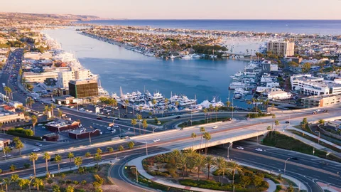 Aerial view of a marina with boats docked, surrounded by roads and buildings near the coast.