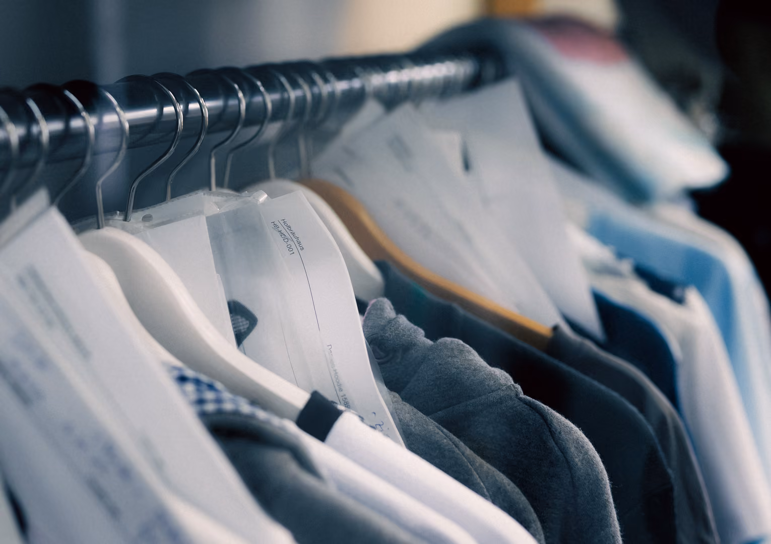 Clothes on hangers in a row on a metal clothing rack with papers attached.