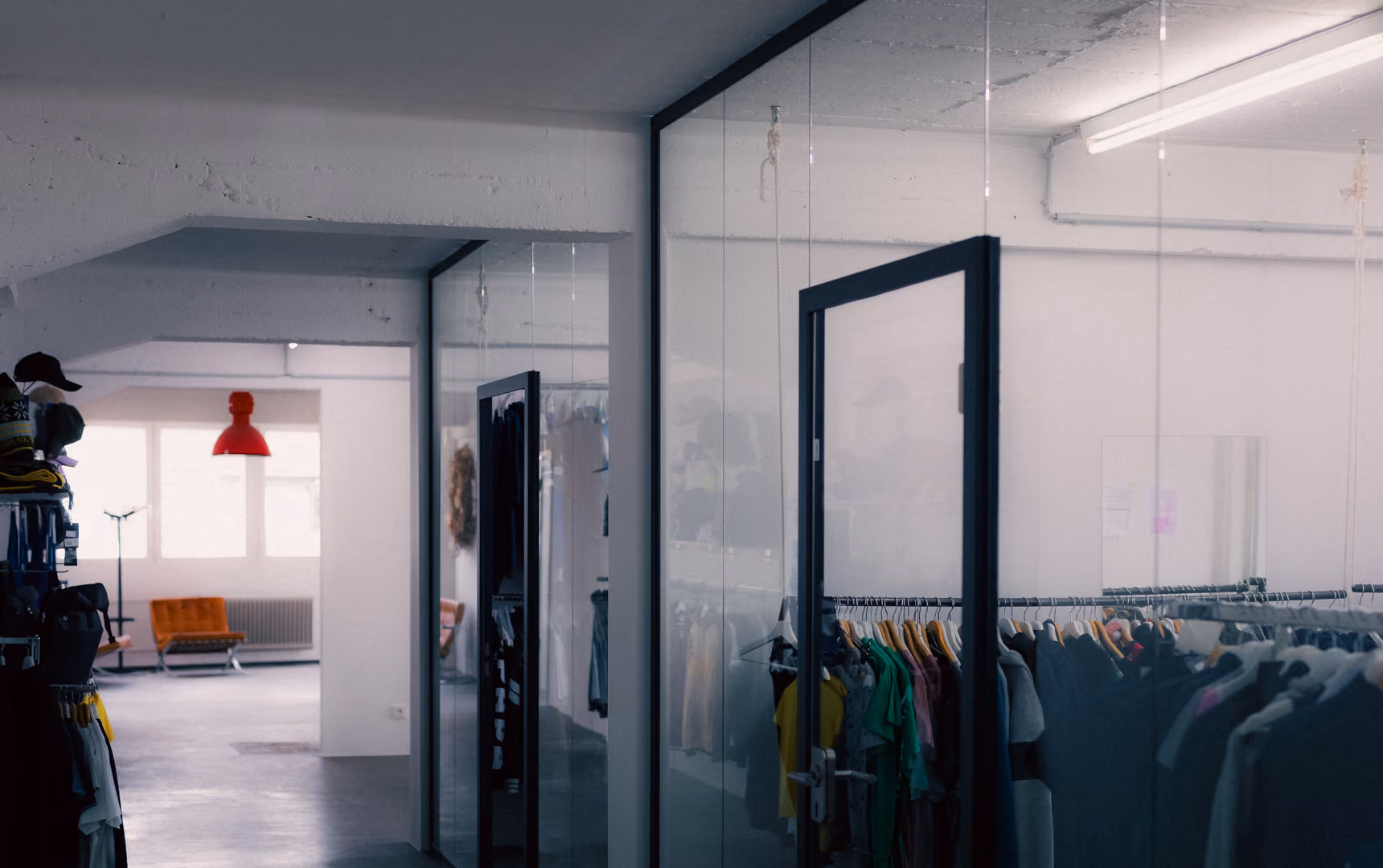 Clothing racks inside a modern store with glass walls and an orange chair near a window.