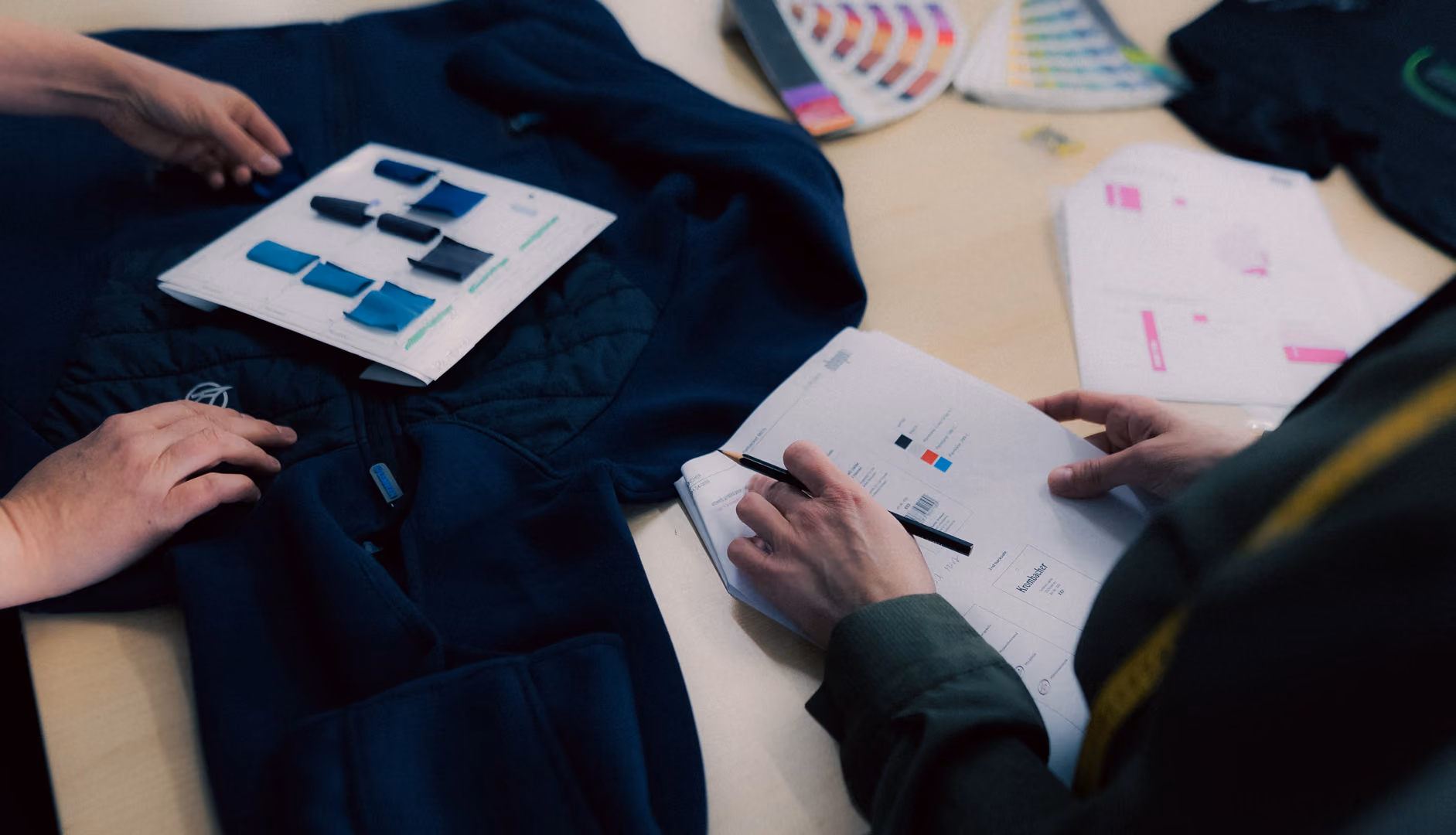 Two people examining color swatches and fabric samples on a dark jacket over a light table.
