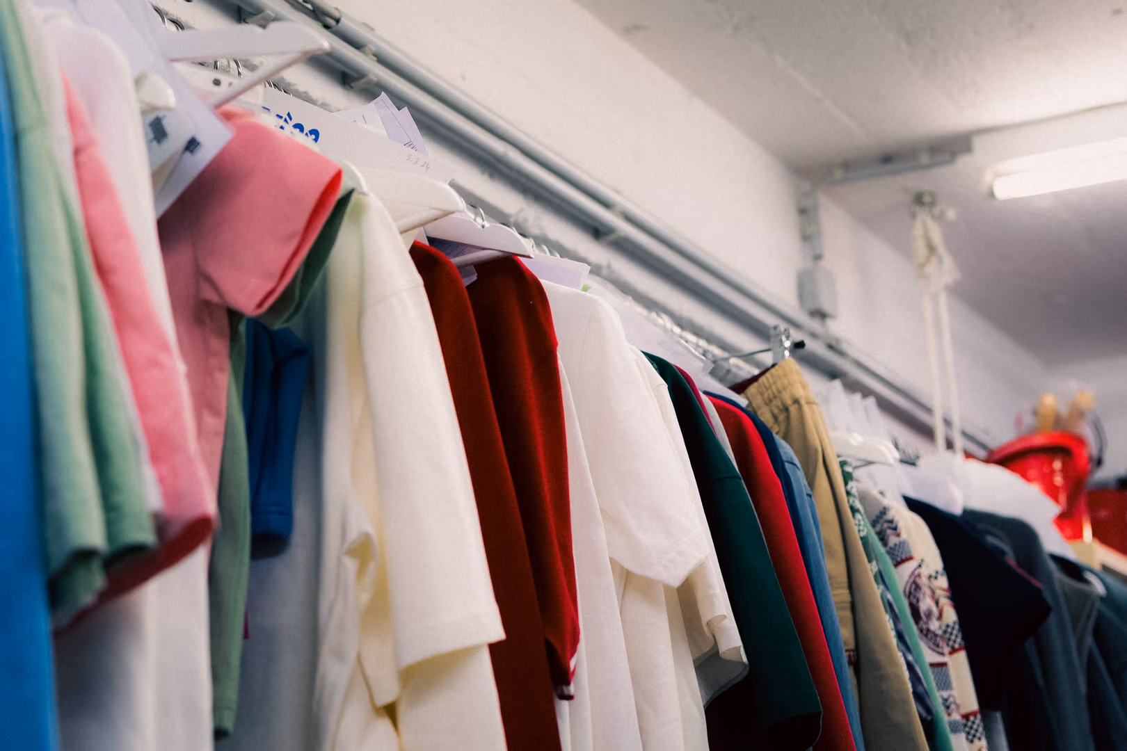 Clothes in various colors hanging on a rack in a room with white walls and ceiling light.