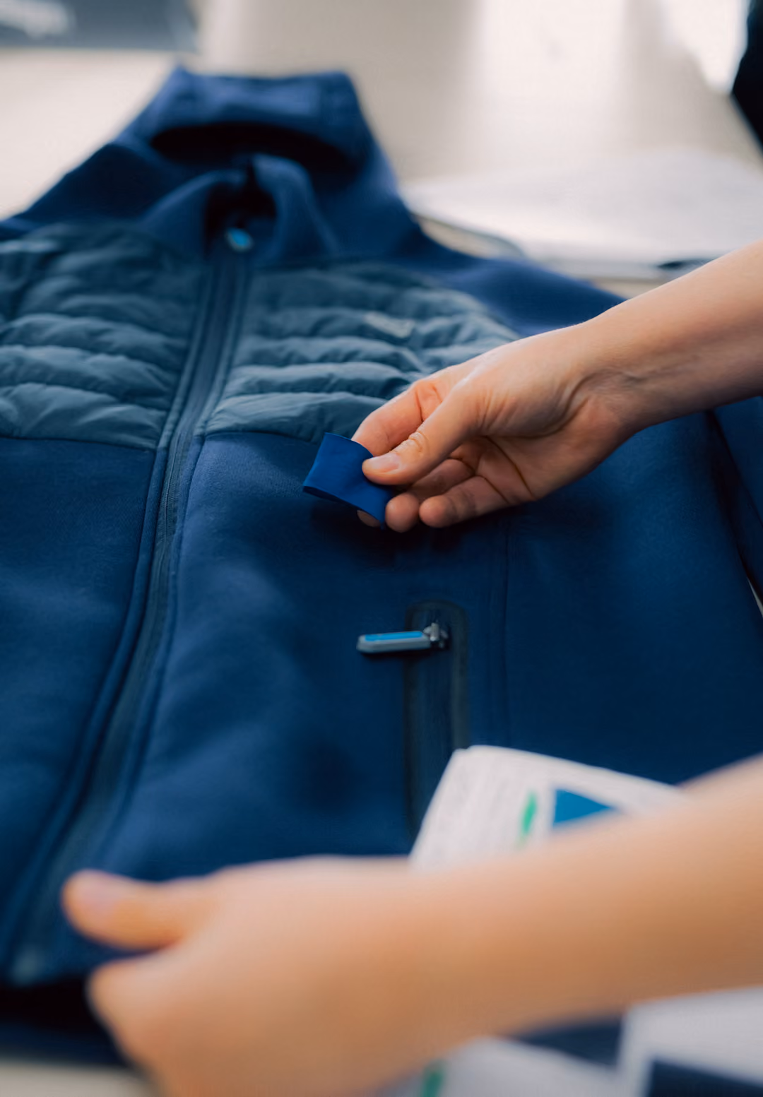 Hands holding a blue fabric strip above a blue jacket with a zipper on a table.